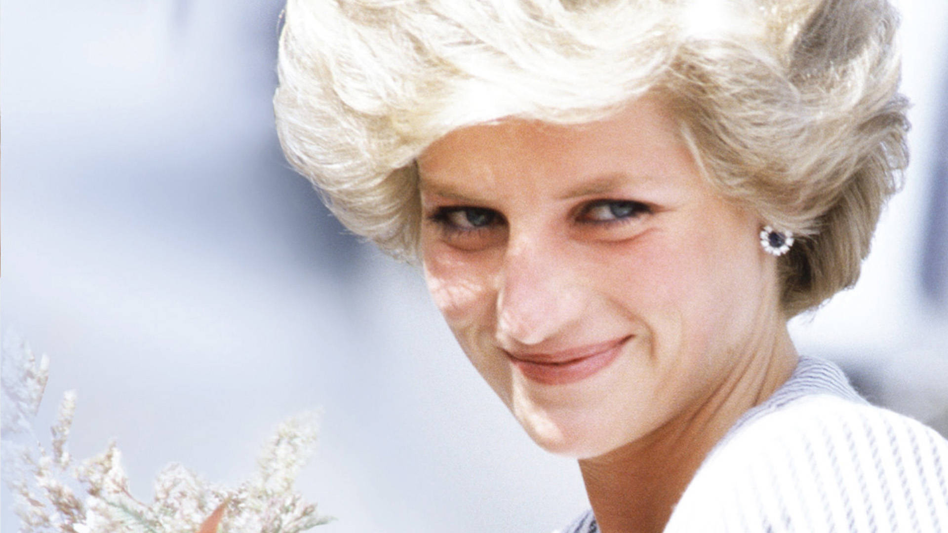 戴安娜王妃微笑著，金色頭髮和珍珠耳環，手持鮮花。
