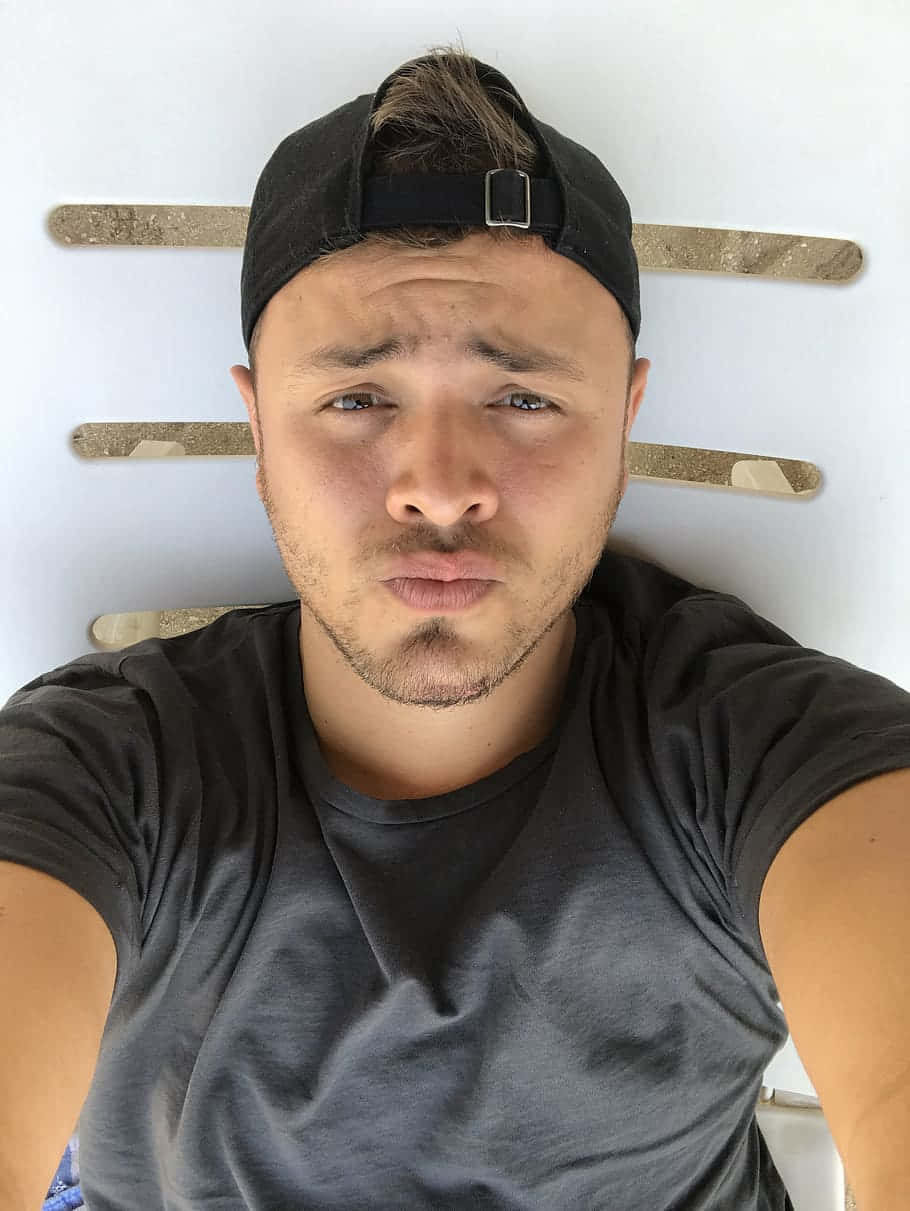 戴著黑色鴨舌帽和灰色T恤的年輕男子，背靠著有木條的白色牆壁躺著。