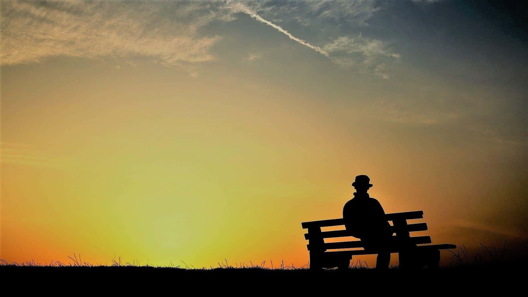 Lonely 桌布 壁紙 — 戴帽子的男人剪影獨自坐在長椅上，背景是帶有縷縷雲彩的鮮豔日落天空。