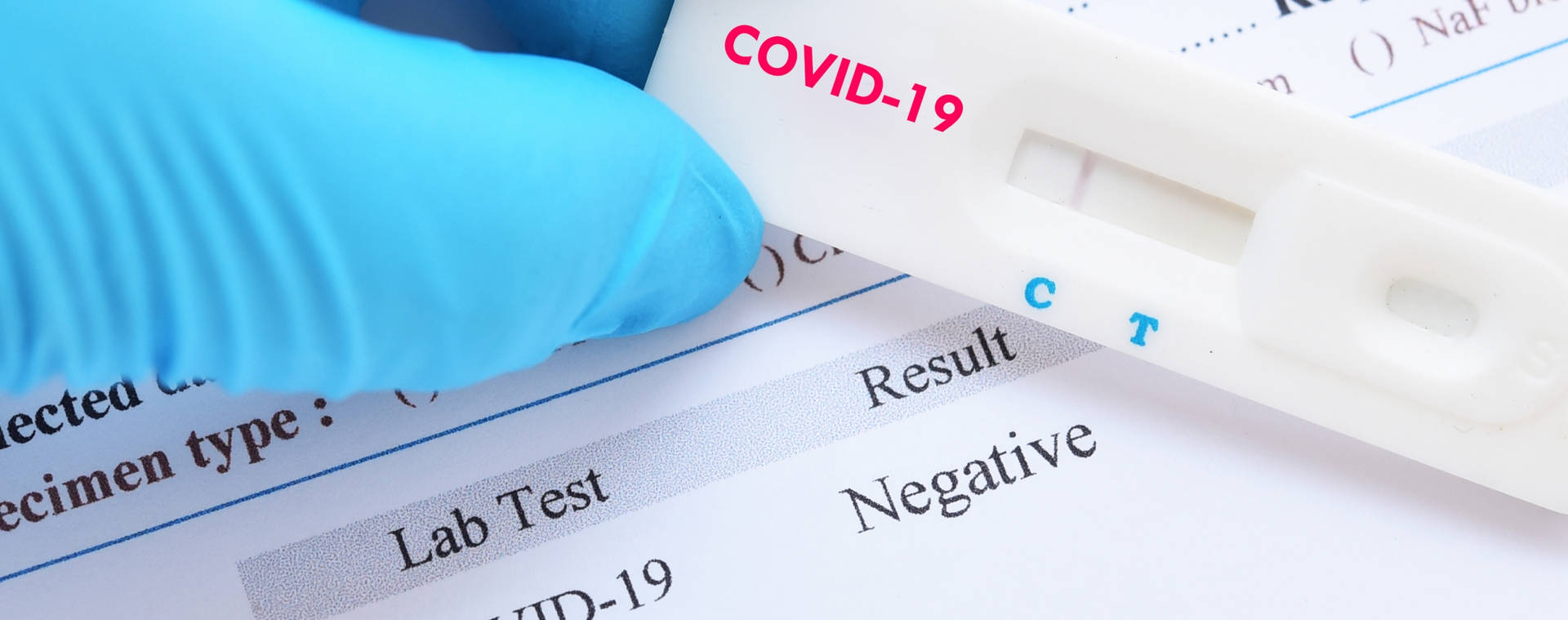 戴著手套的手在實驗室報告上拿著陰性的COVID-19測試條。