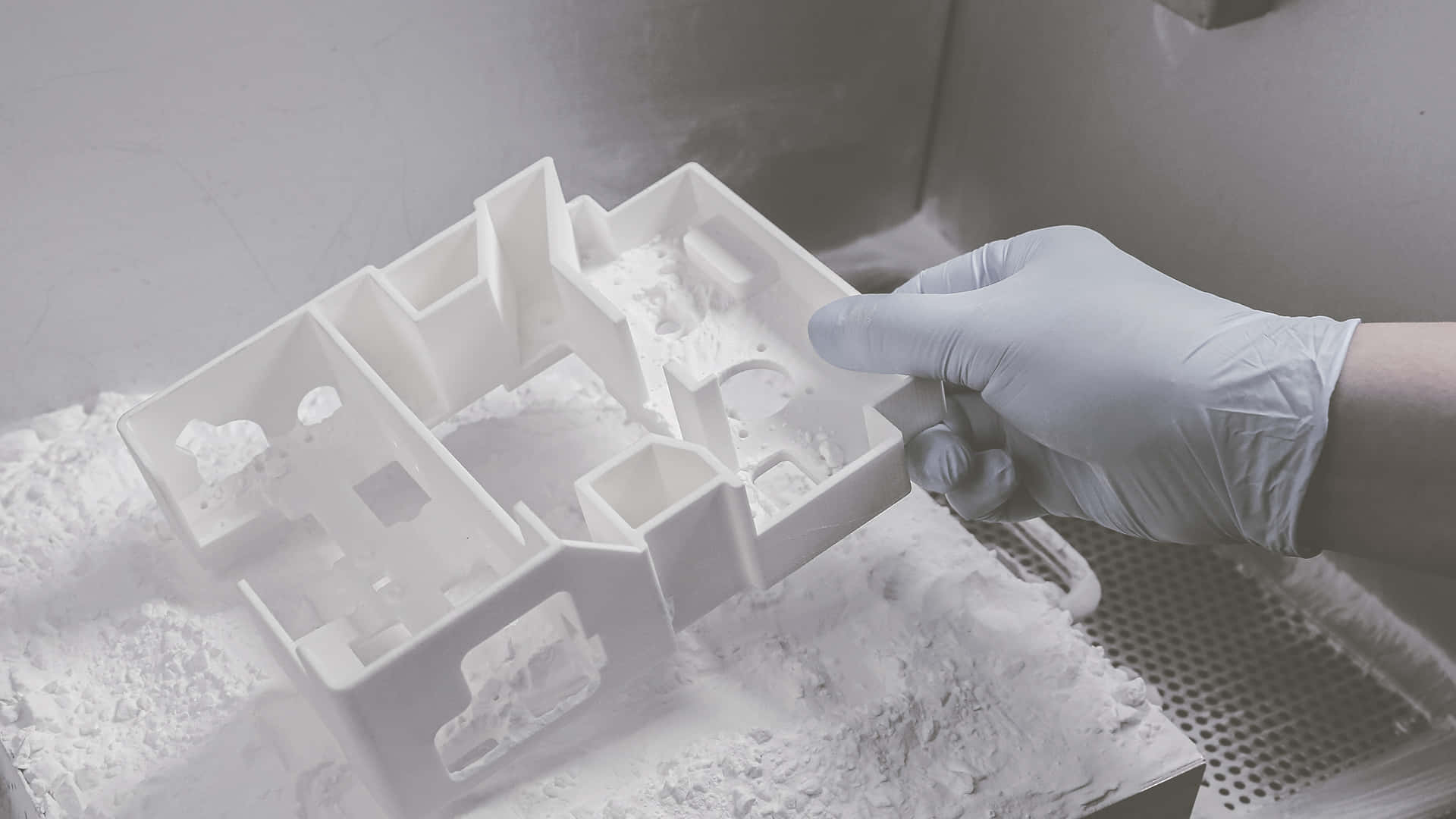 3d Printer 桌布 壁紙 — 戴手套的手從無塵室環境中的粉末床上拿起一個白色3D打印建築模型。