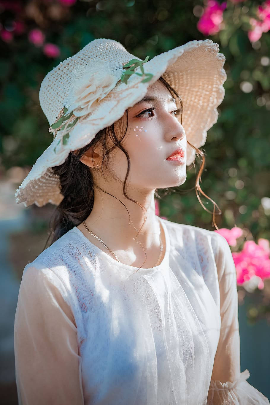 戴白色帽子和襯衫的女子站在陽光下的粉紅花朵中。