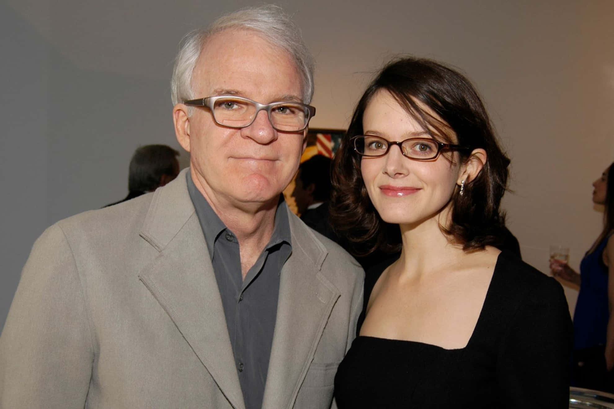 steve martin 桌布 壁紙 — 戴眼鏡嘅男人同女人喺室內柔和燈光下嘅社交聚會一齊微笑。