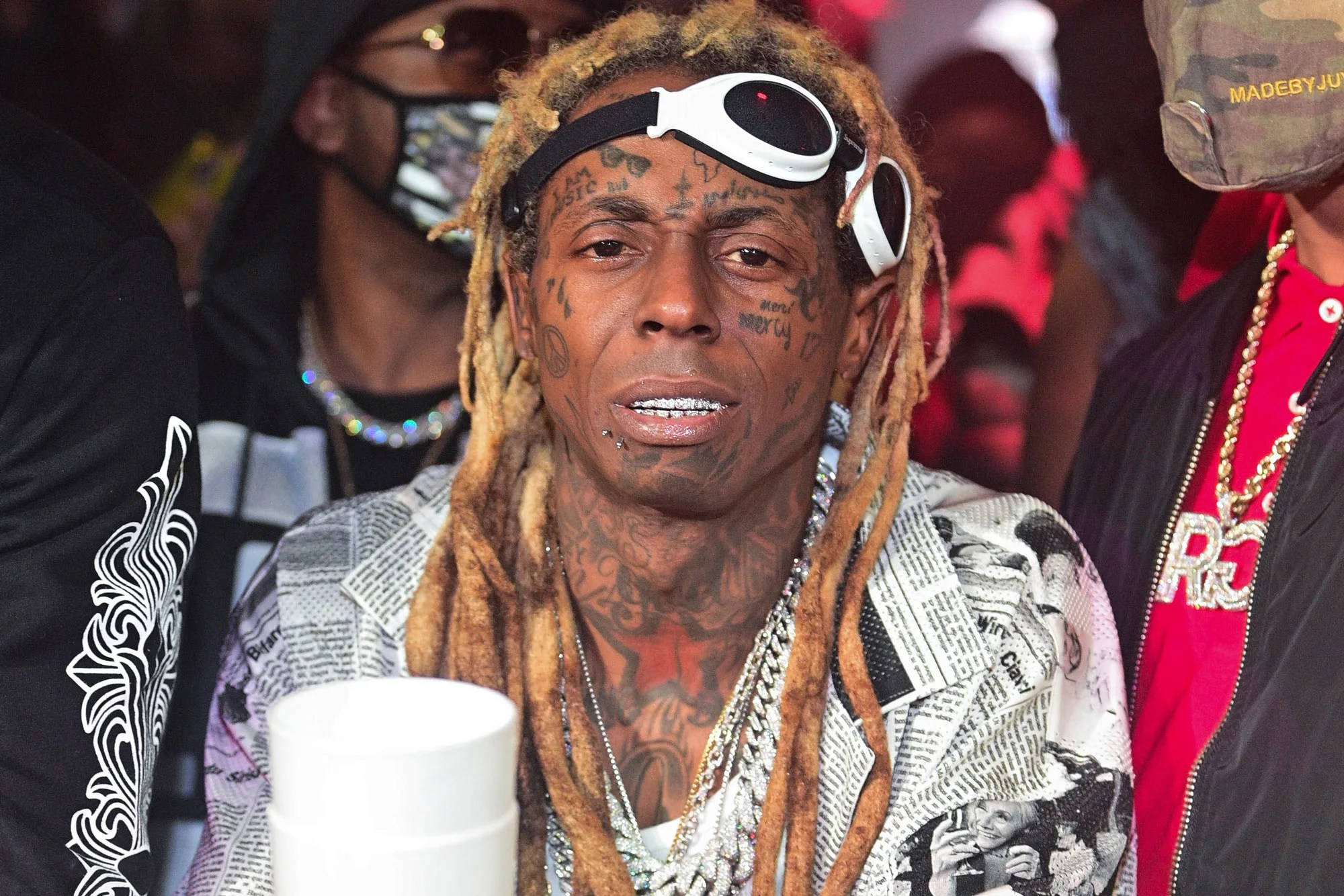 戴眼鏡的 Lil Wayne 壁紙 — Lil Wayne 頭戴白色護目鏡，身穿報紙印花外套，在活動中被人群包圍。