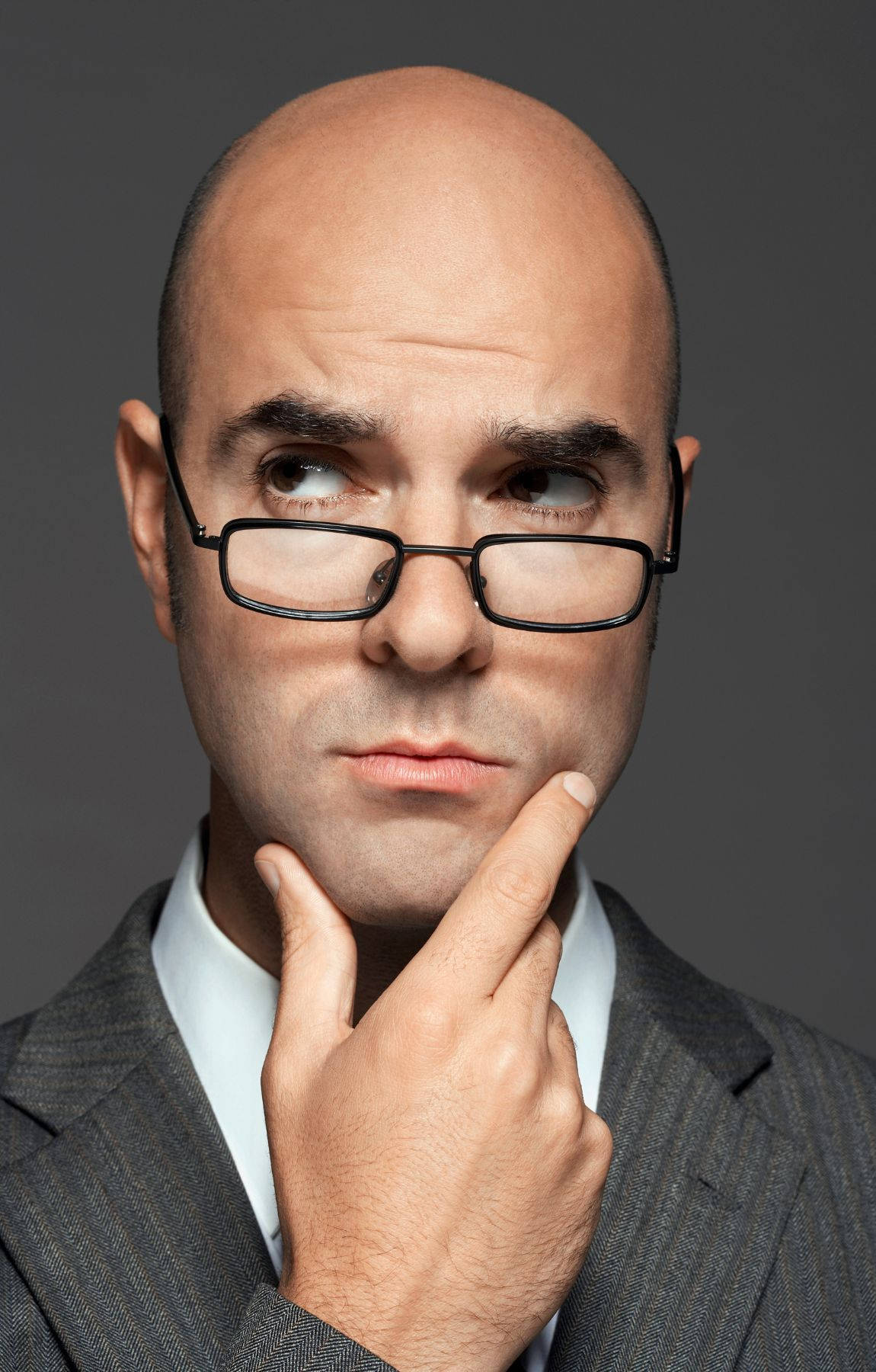 光頭戴眼鏡穿西裝的男人，手托下巴思考。