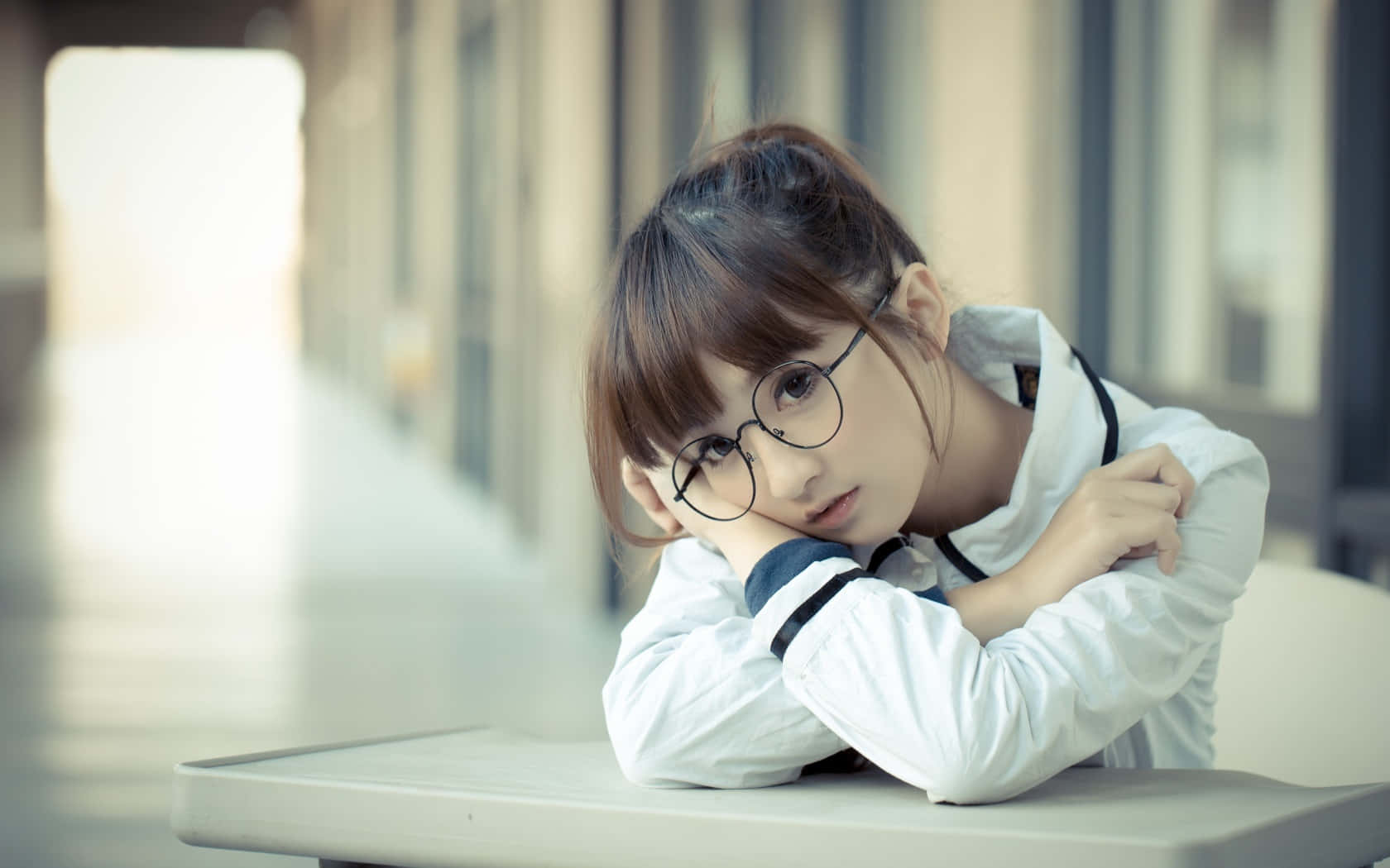 一位戴眼鏡的年輕女子在室內的桌子上將頭靠在手臂上休息。