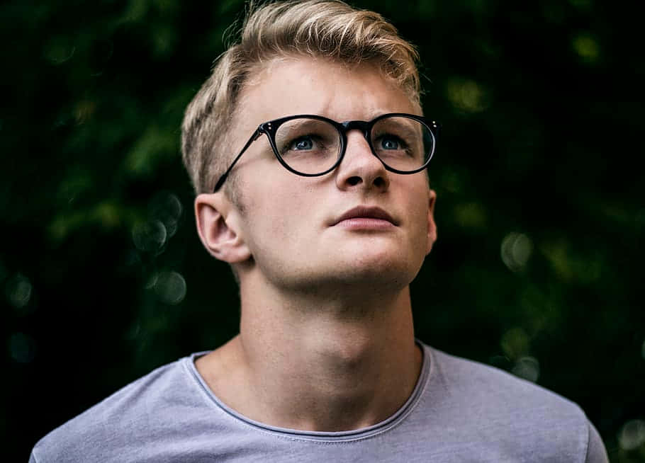 戴眼鏡的年輕男子在綠色樹葉中若有所思地向上看。