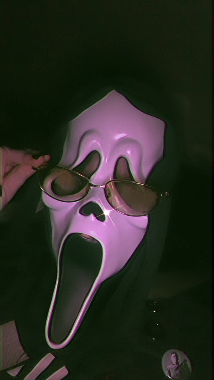 一個粉紅色 Ghostface 面具，配金色框太陽眼鏡，喺黑暗嘅綠色燈光下。