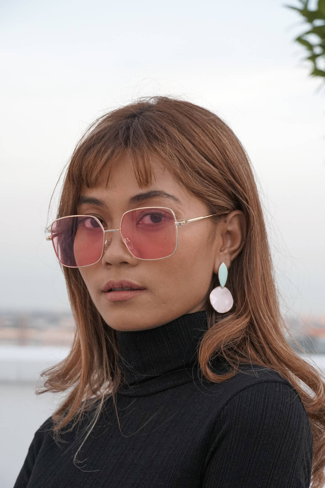 戴著粉紅色太陽眼鏡、身穿黑色高領毛衣和粉彩耳環的女性。