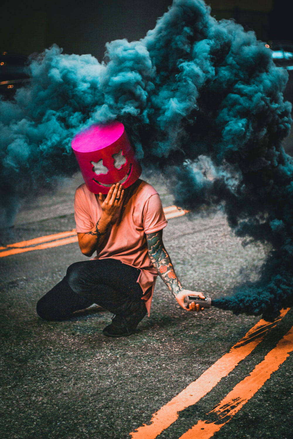 戴粉紅桶頭單身男孩 壁紙 — 一個人戴住粉紅色笑面桶形頭盔跪喺街上，用手提裝置釋放出藍綠色煙霧。