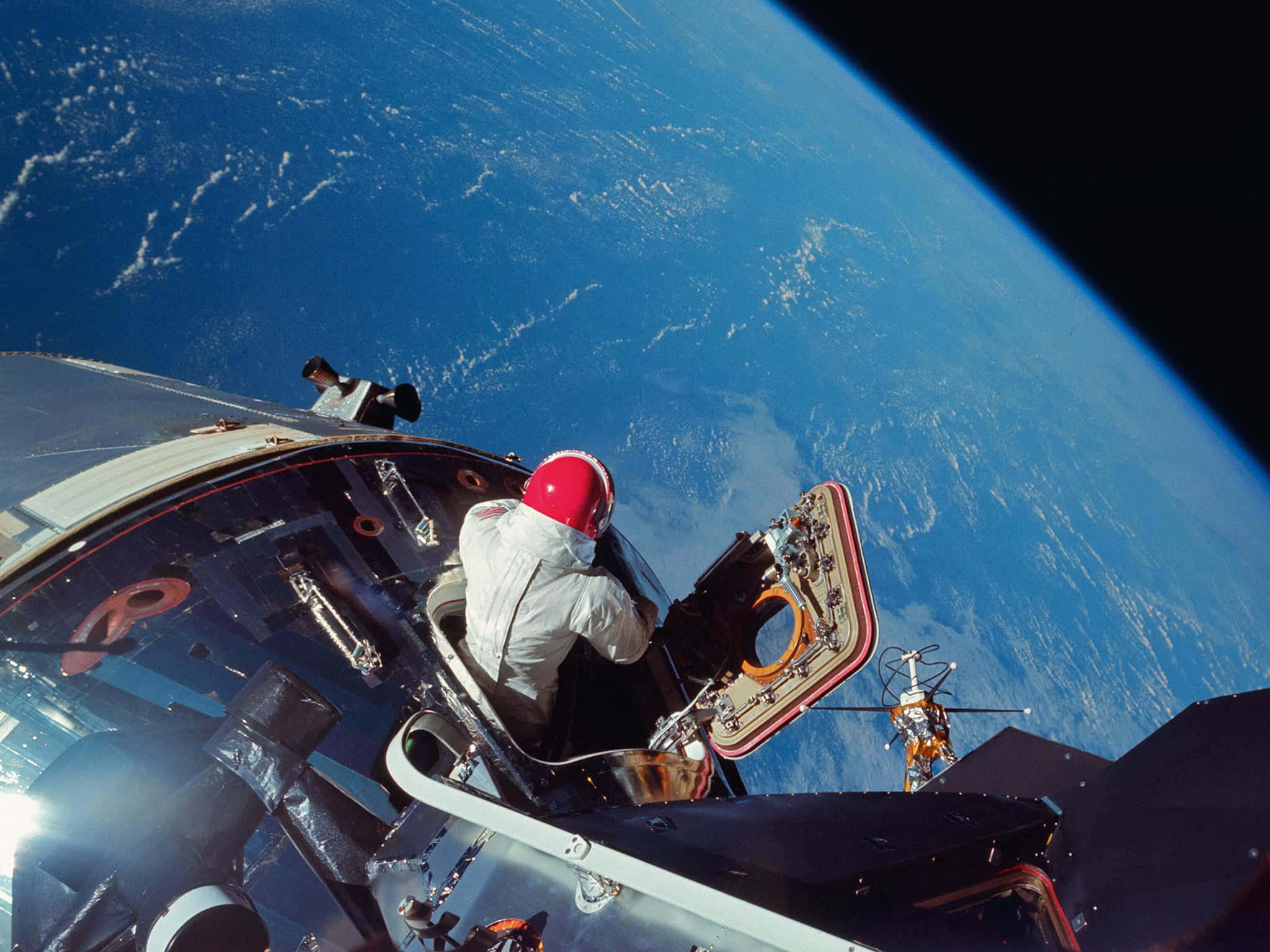 Space Exploration 桌布 壁紙 — 戴紅色頭盔的太空人在太空船外進行太空漫步，下方可見地球的藍色曲線和白色雲層。