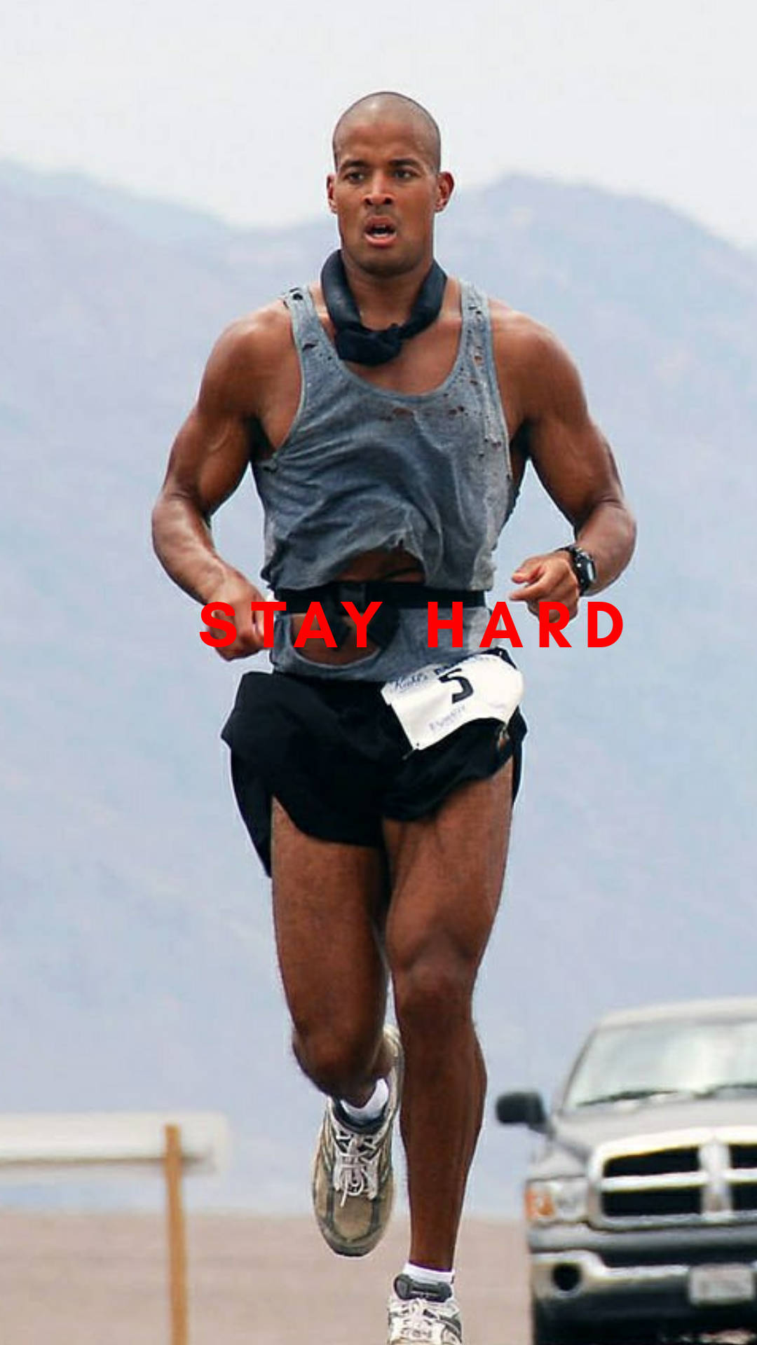一位男性跑者在比賽中，胸前印有「STAY HARD」字樣，背景為山區地形。