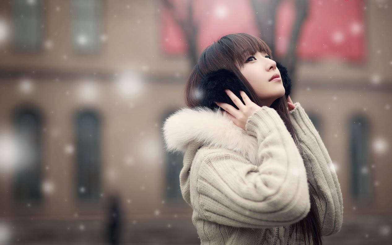 穿著冬季大衣的女子在城市中仰望飄落的雪