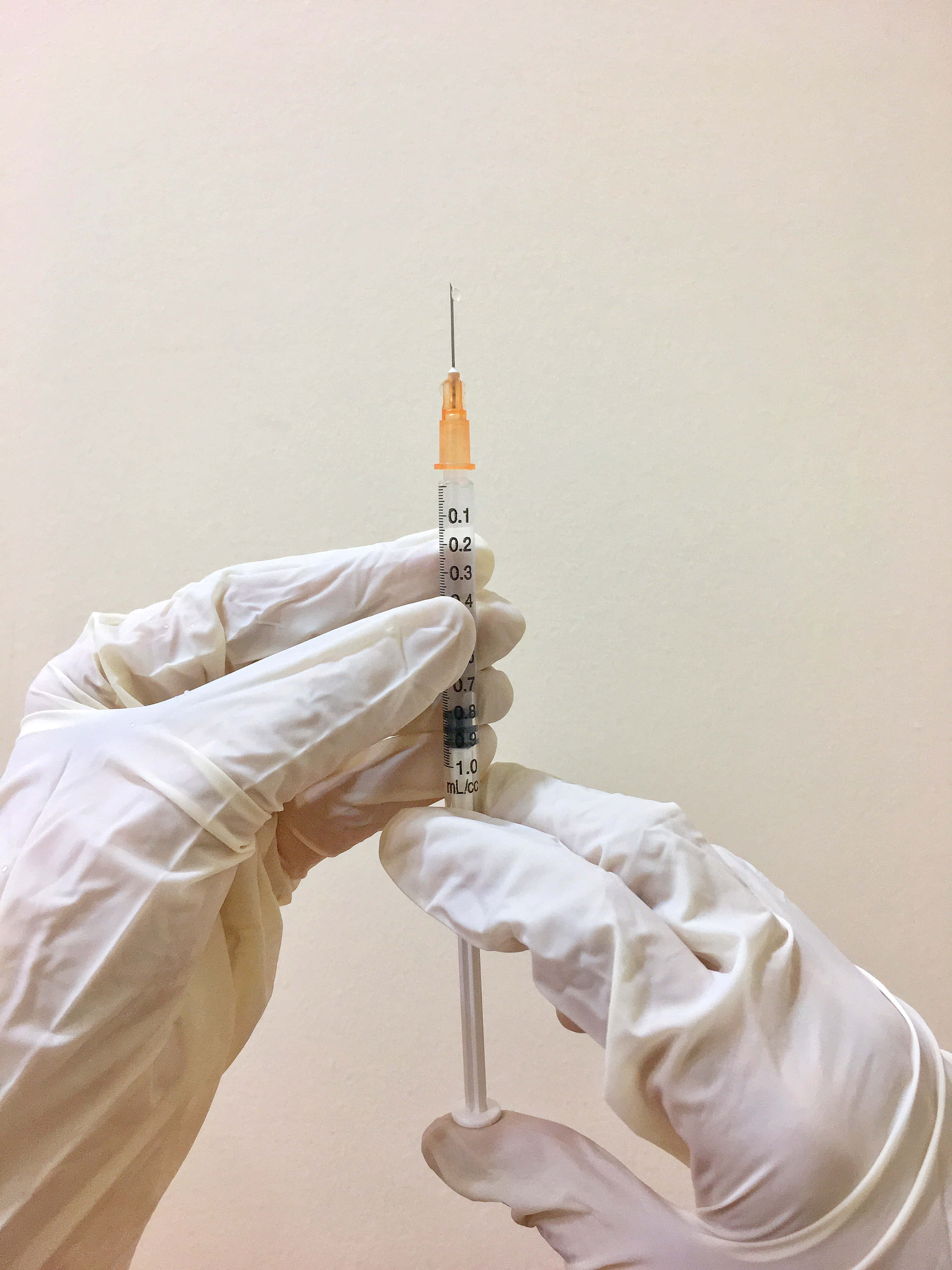 Sick 桌布 壁紙 — 戴著手套的手握著一支醫療注射器，針頭準備好注射，背景是純色米色牆壁。
