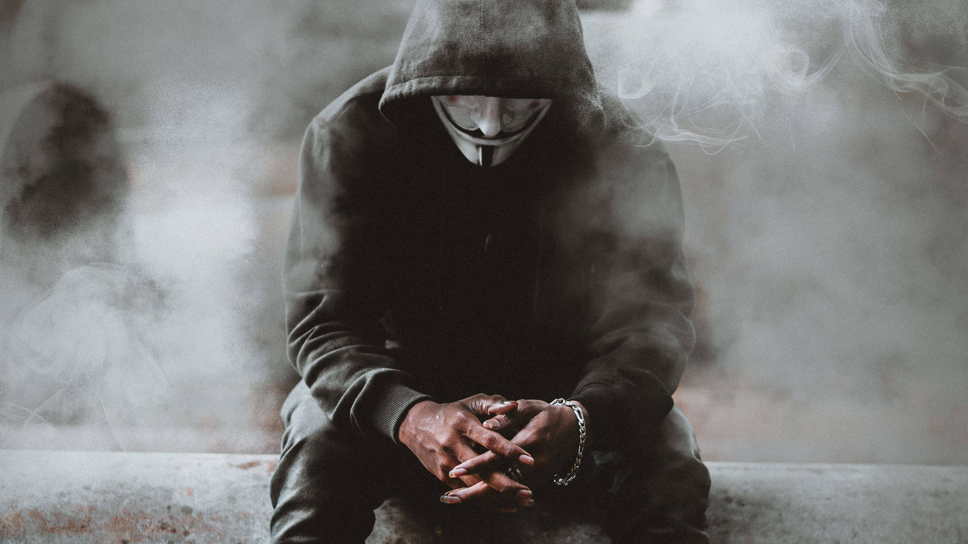 穿連帽衫和蓋伊·福克斯面具的人坐在煙霧中，雙手緊握。