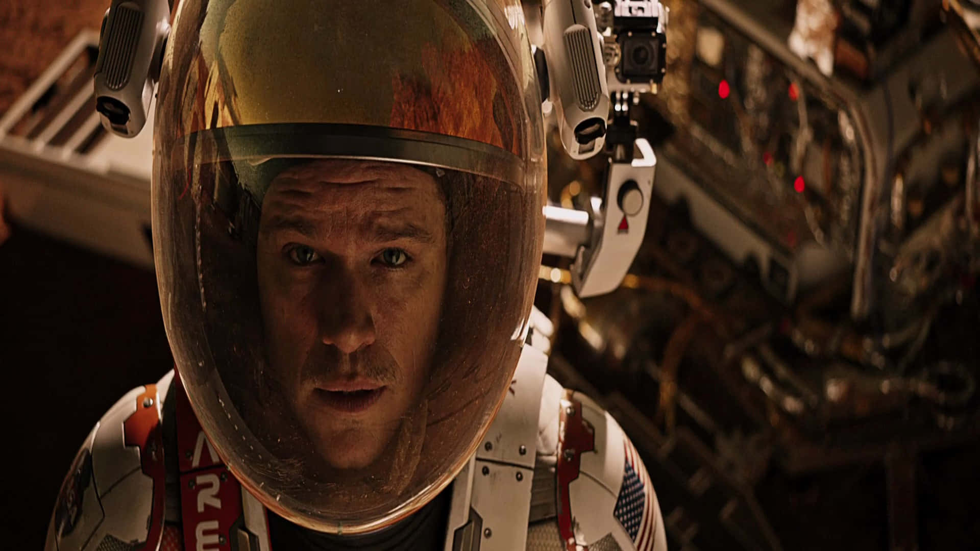 The Martian 桌布 壁紙 — 戴著頭盔的太空人專注地凝視，背景有太空船和紅光。