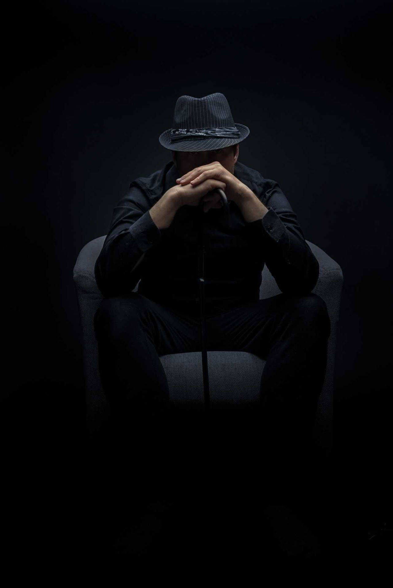 一個身穿斗篷、頭戴軟呢帽的男人坐在陰影中，雙手放在臉上。