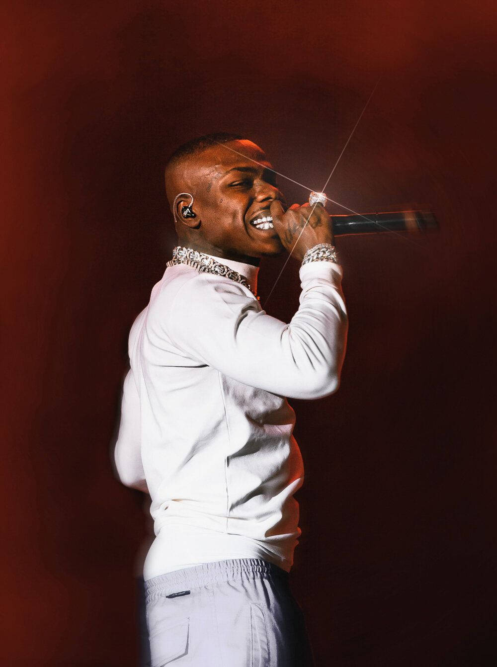 戴鑽戒演出 DaBaby 手機 壁紙 — 一位微笑的男饒舌歌手身穿白色服裝，在紅色燈光下拿著麥克風充滿活力地在舞台上表演。