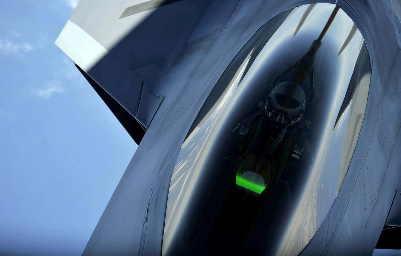 戴黑頭盔駕駛員駕駛戰鬥機 壁紙 — 戰鬥機駕駛艙內的低角度視圖，飛行員戴著頭盔，發光的綠色儀表板映襯著清澈的藍天。