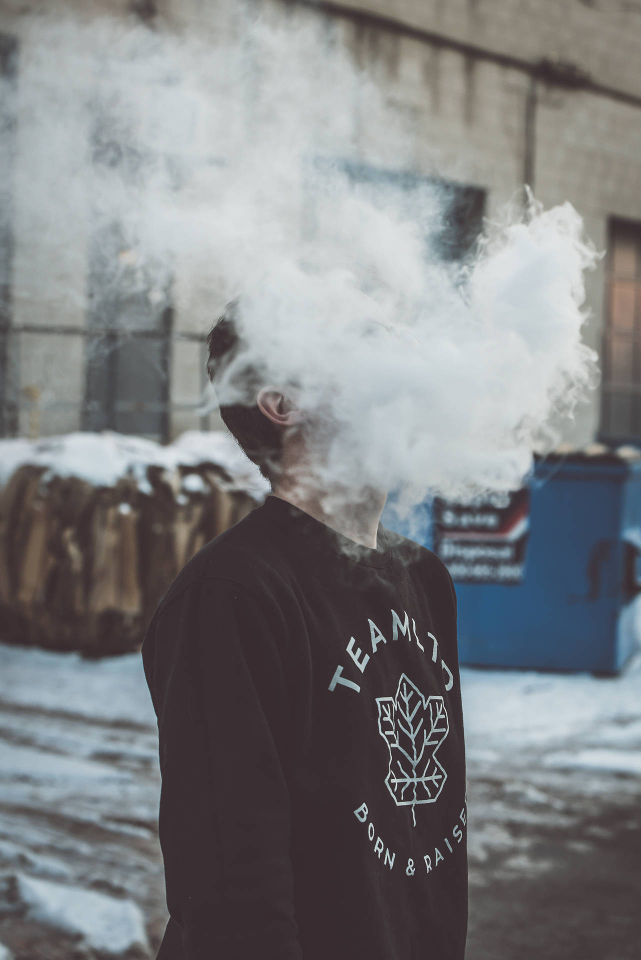 在雪白城市環境中穿著黑色運動衫呼出蒸氣的人