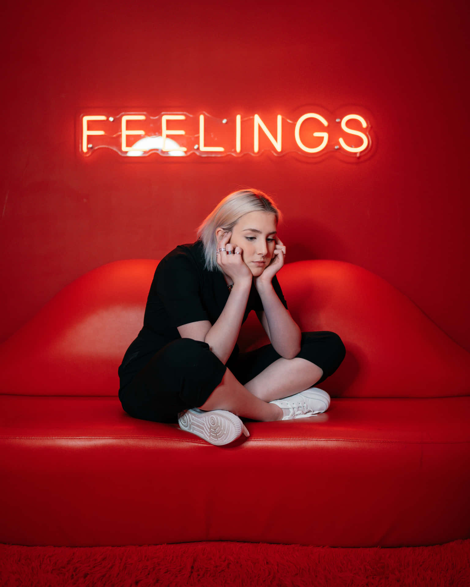 人坐在紅色梳化上，紅色霓虹燈牌寫著 FEELINGS。