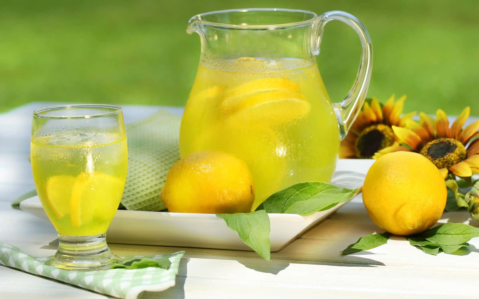 Refreshing 桌布 壁紙 — 戶外白色木桌上，一杯及一壺清涼檸檬水，配以原個檸檬和向日葵。