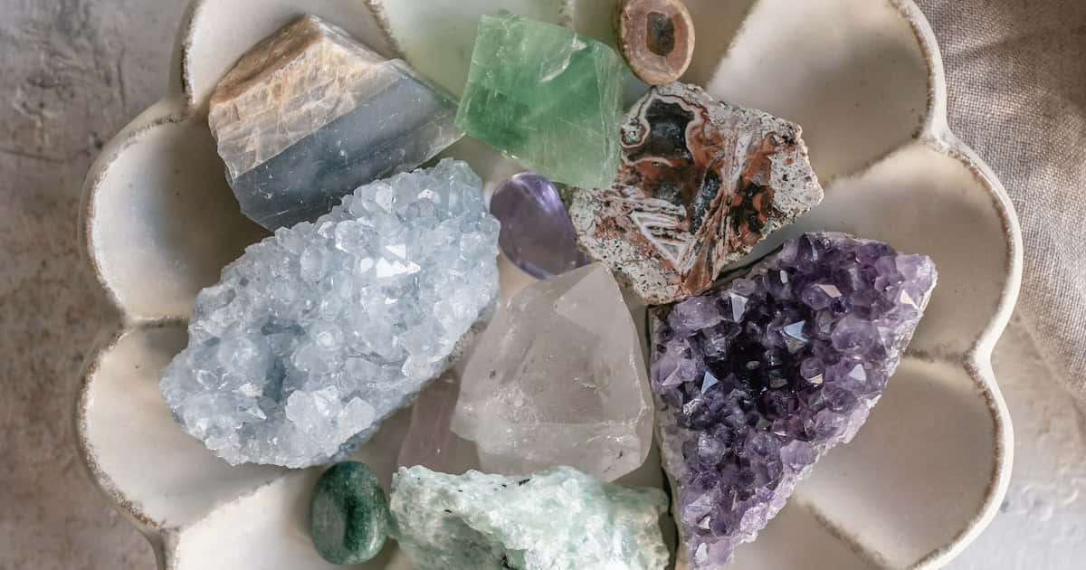 房間中央閃耀的晶體 壁紙 — 一個陶瓷花形碟子盛載著色彩鮮豔的各種水晶和石頭，包括紫水晶石英和綠色螢石。