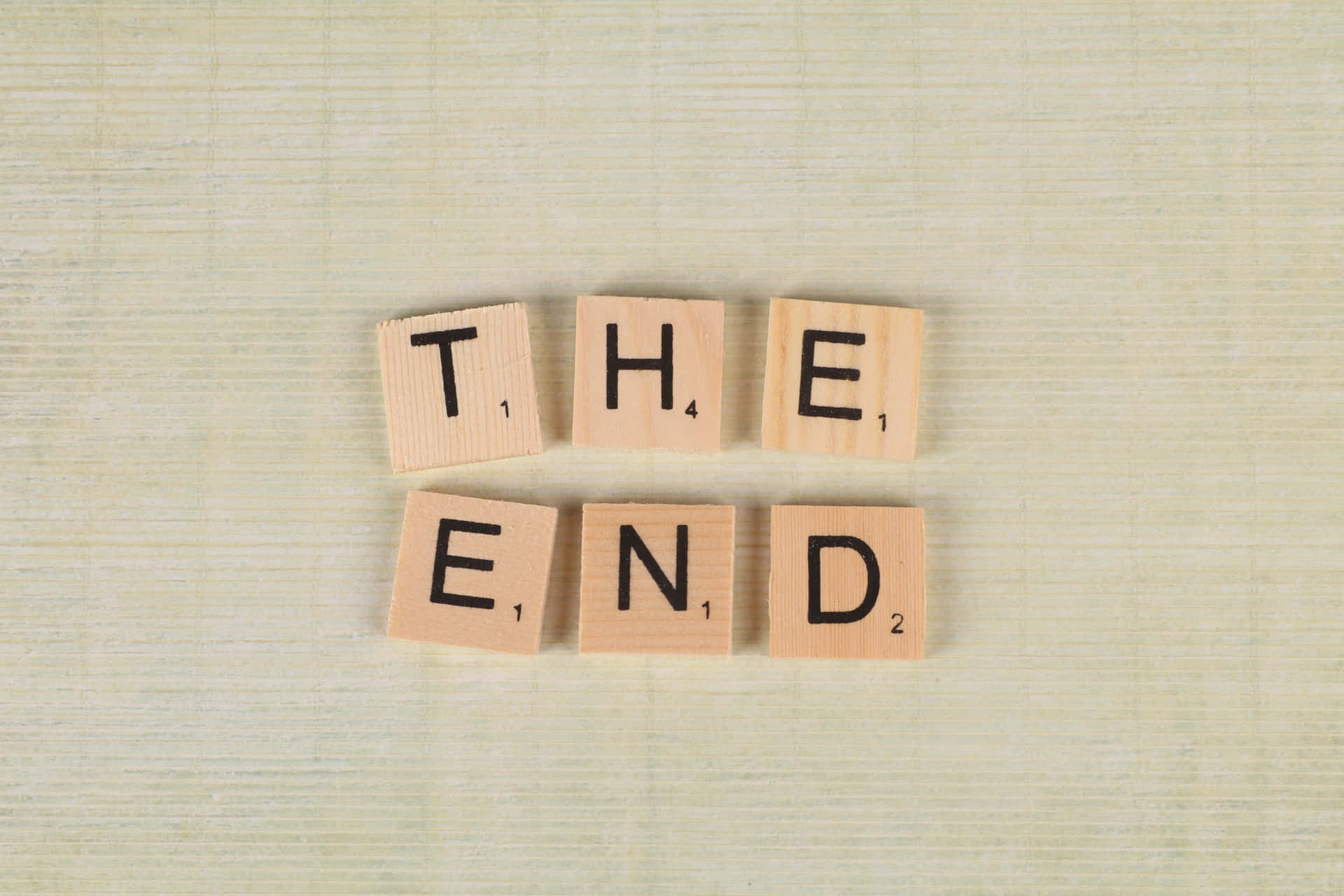 木製 Scrabble 字母牌在米色紋理背景上拼出 the end。