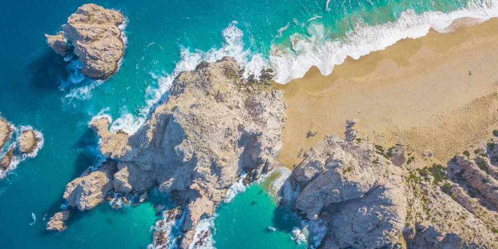 從高空拍攝，碧綠色的海浪沖擊沙灘和懸崖。