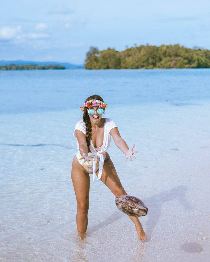 戴太陽眼鏡和花冠的女性在熱帶沙灘上踢椰子。