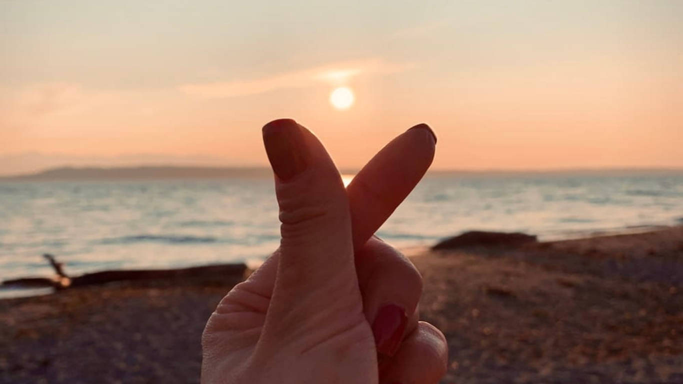 在海洋海灘日落時做出和平手勢的手