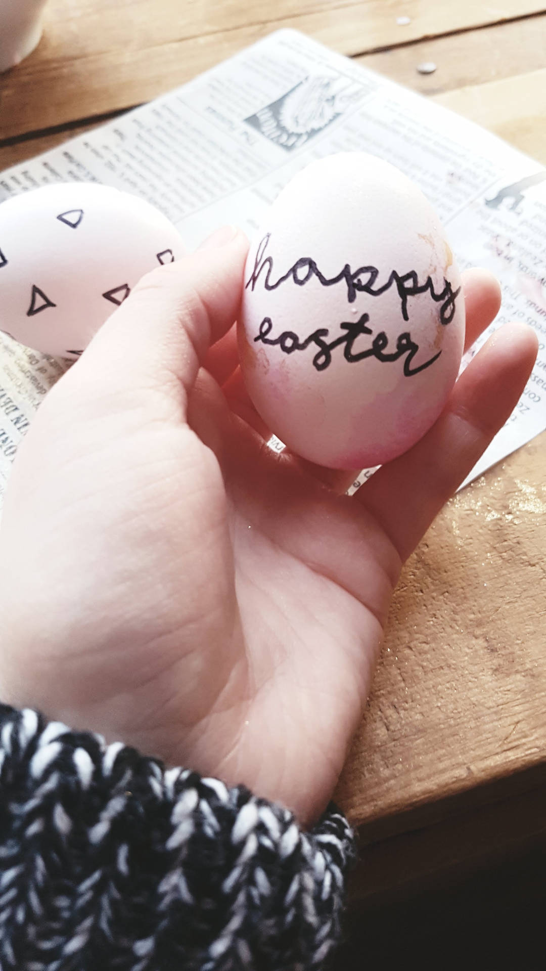 手拿著裝飾復活蛋，上面有 'happy easter' 文字，放在木桌上。