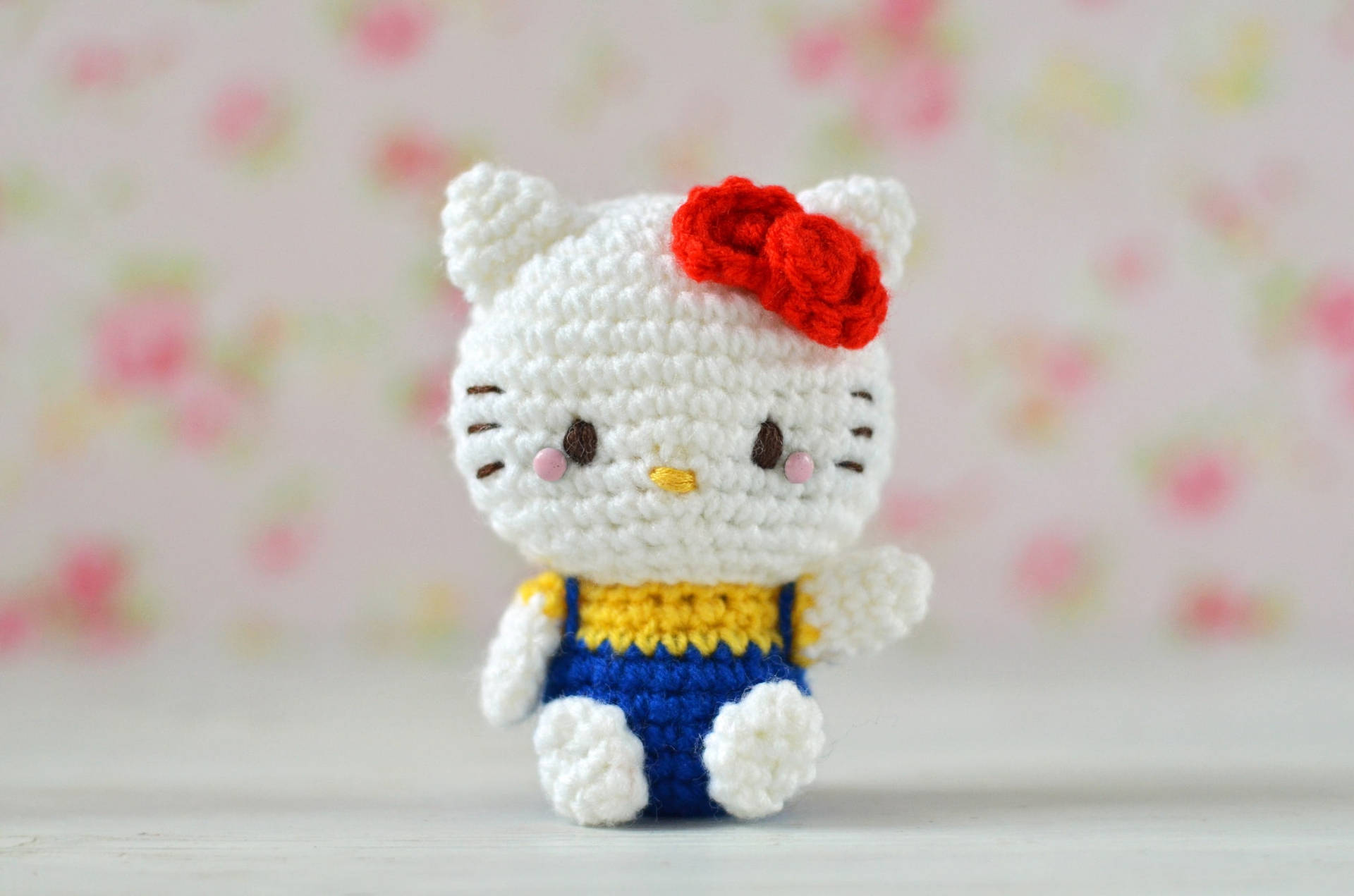 一個鉤針編織的Hello Kitty公仔，穿著藍色吊帶褲和紅色蝴蝶結。