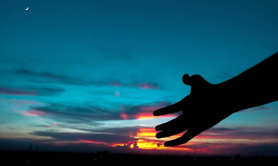 手影夕照雲朵美學桌面壁紙 壁紙 — 一隻剪影手伸向充滿活力的日落天空，上方有一彎新月。