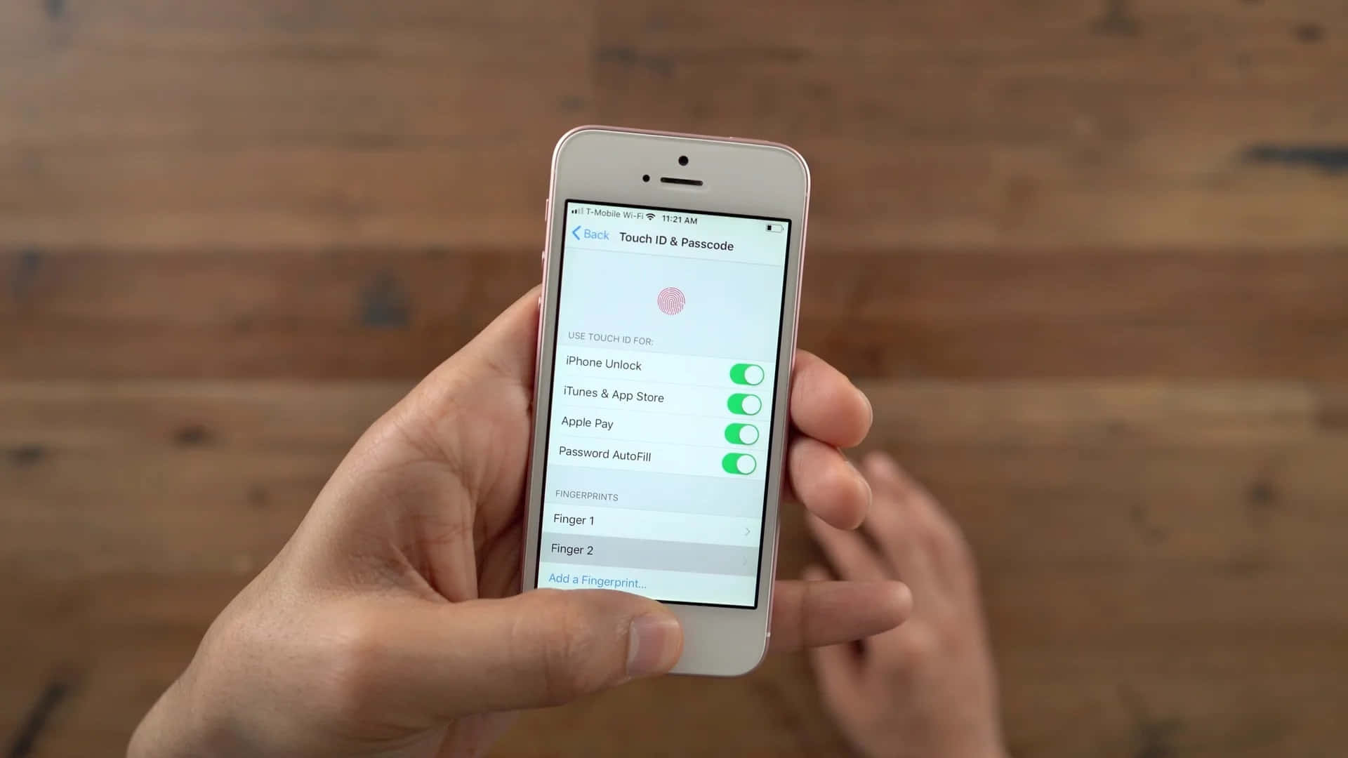 Touch Id 桌布 壁紙 — 手拿著玫瑰金色iPhone，在溫暖的木質背景上顯示Touch ID設定。