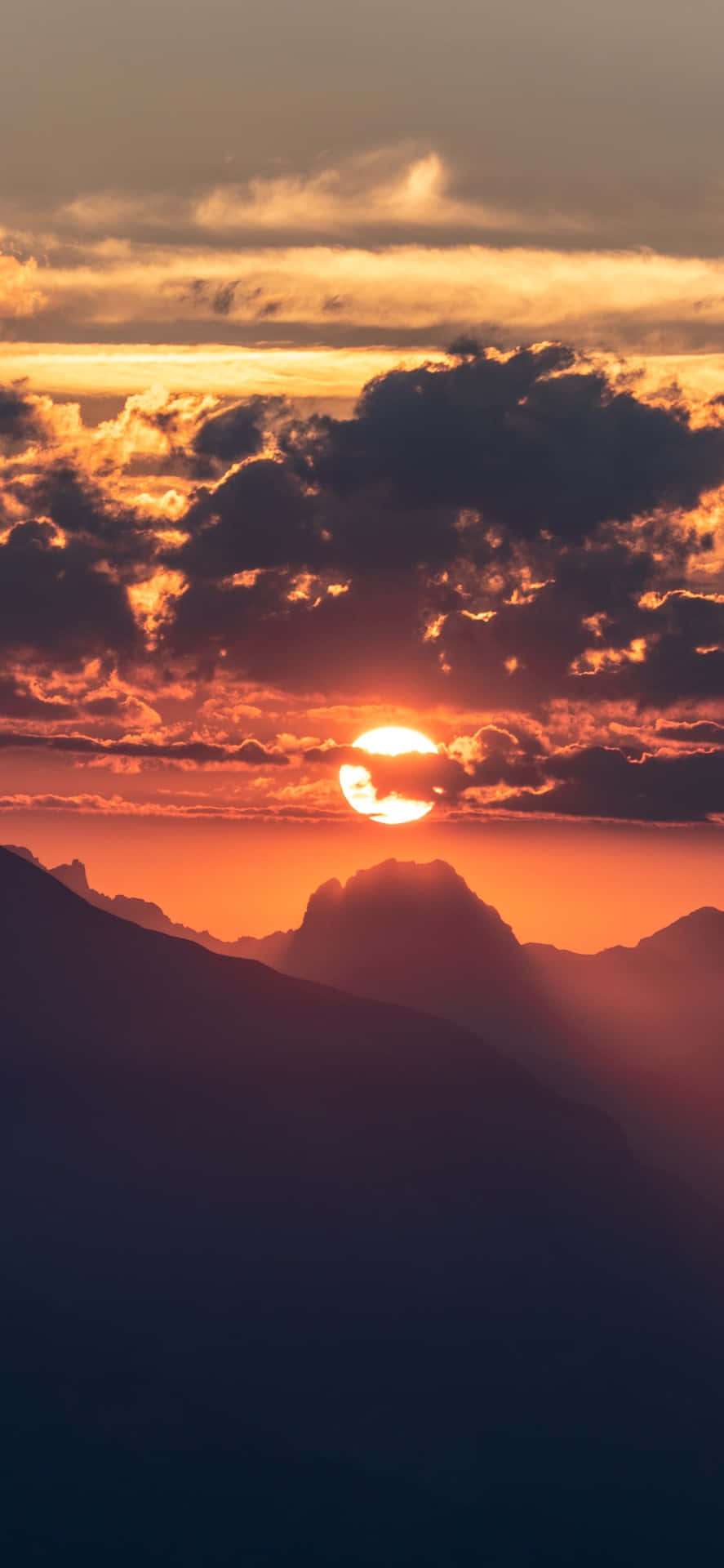 夕陽映照山巒，天空呈現橙色和紅色，伴隨深色雲層。