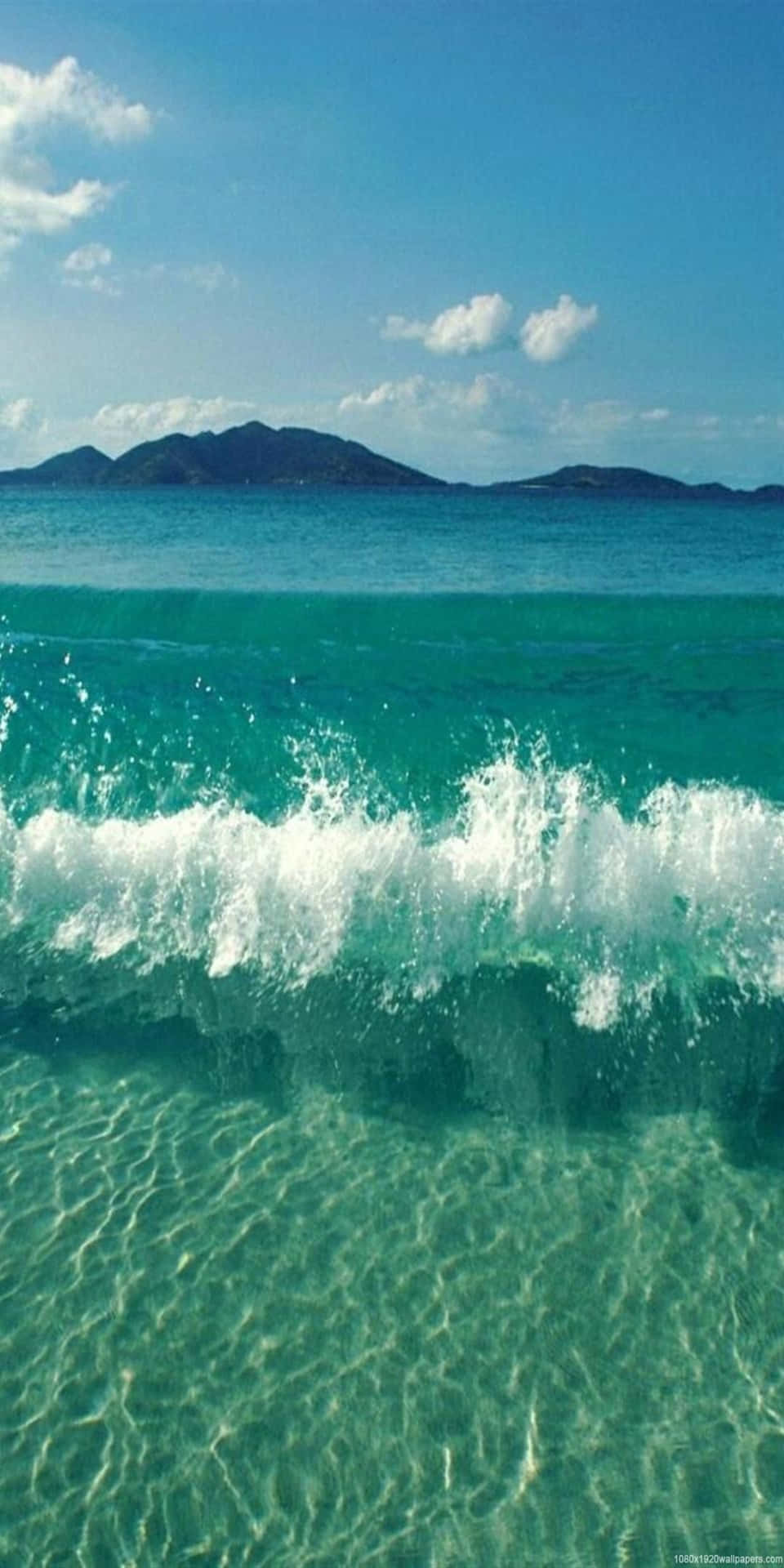 綠松石色的海浪拍打在清澈的淺水上，遠山在背景中。