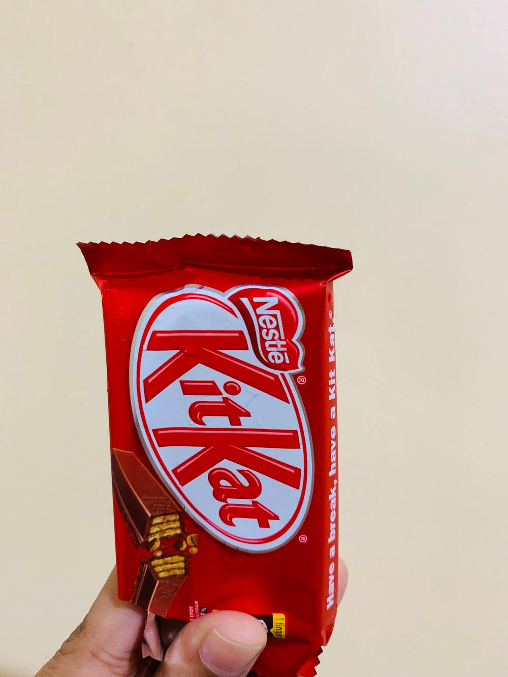 手持KitKat巧克力 壁紙 — 一隻手拿著一條鮮紅色的KitKat朱古力棒，背景是純米色。