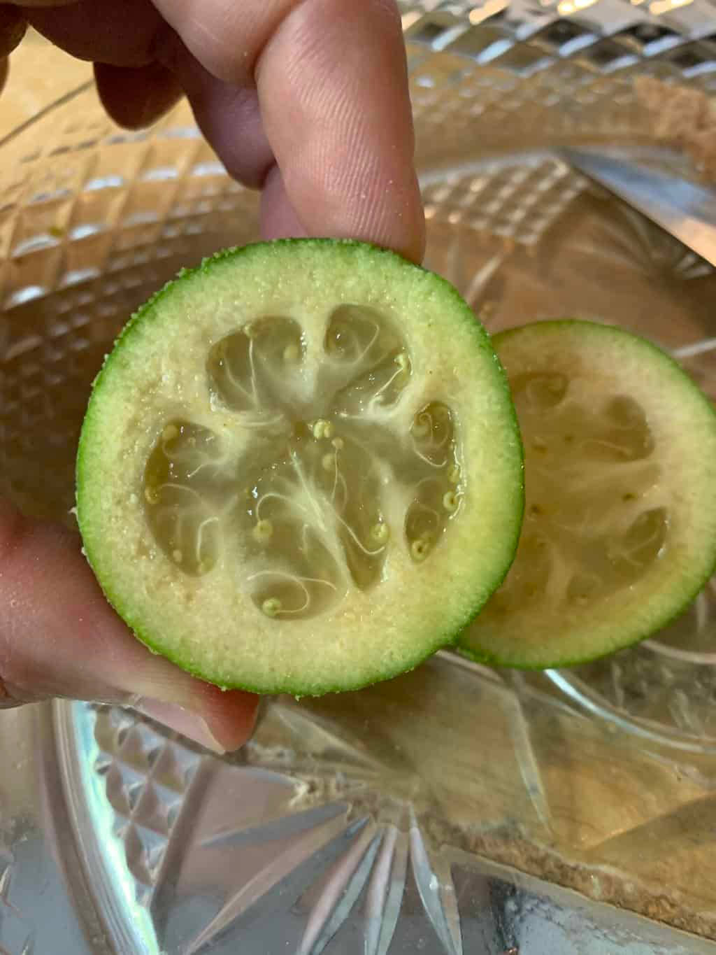 手持一片 Feijoa（菠蘿番石榴） 壁紙 — 一隻手拿著一片切開的青檸，露出多汁的分瓣內部，放在有圖案的玻璃碟上。