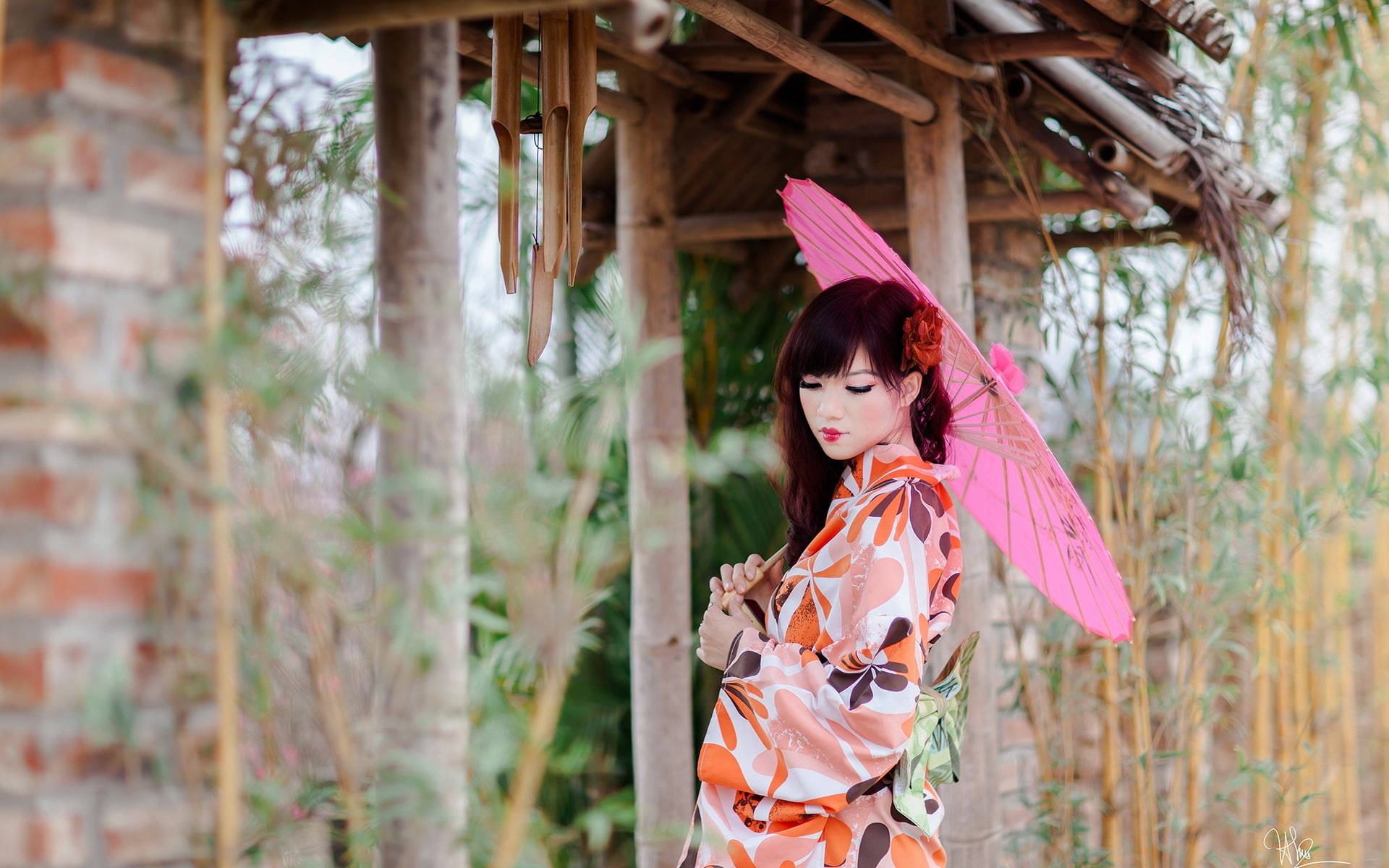 身穿花卉和服的女士在竹亭下撐著粉紅色陽傘。