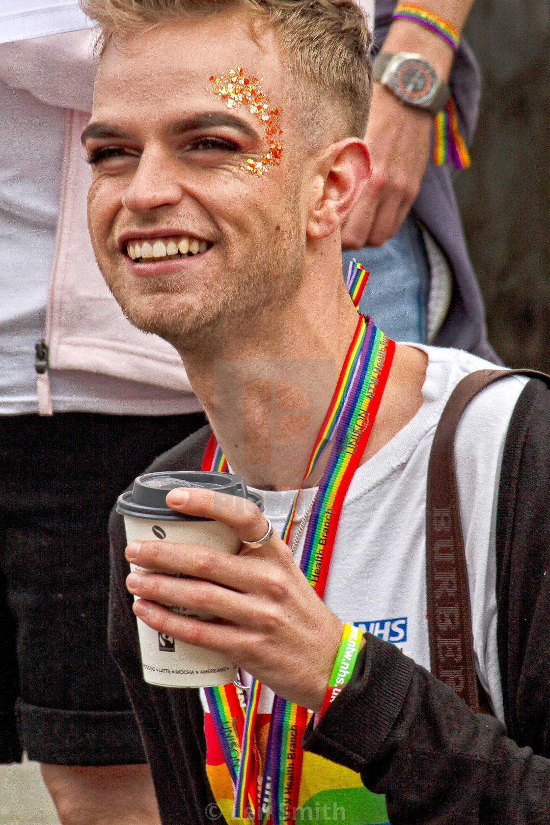 戴著彩虹掛繩和閃粉的男人在Pride遊行中拿著咖啡微笑。