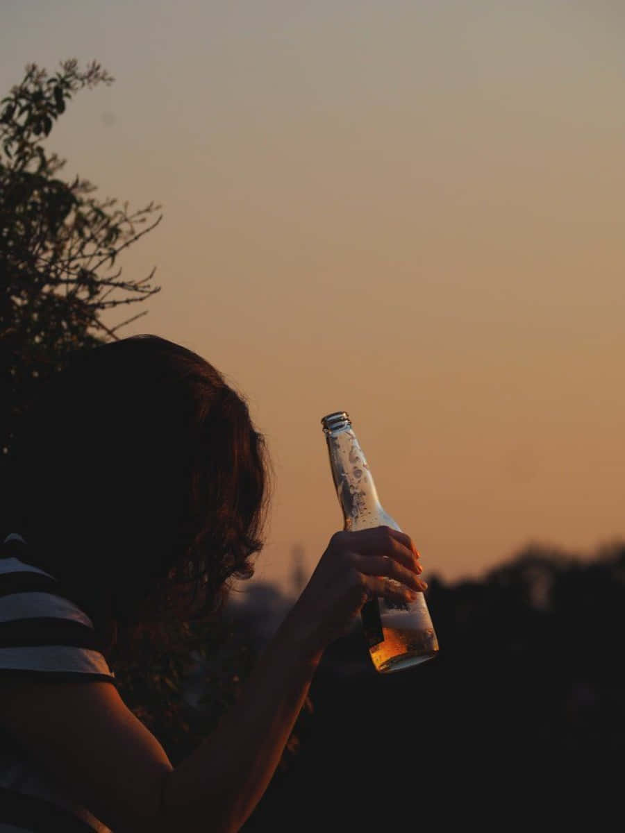 日落時手持啤酒瓶的人與樹木剪影