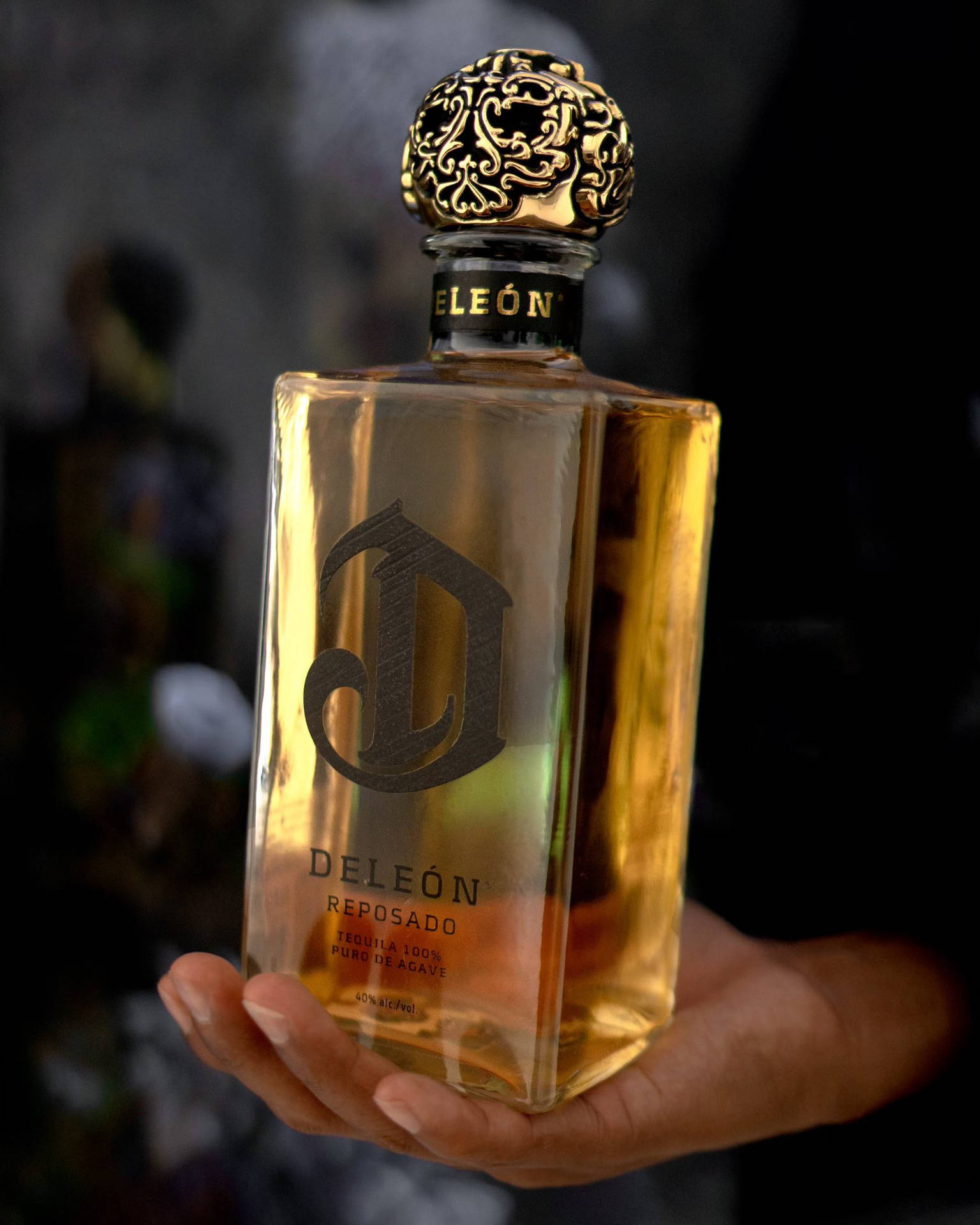 手拿著一個金色的Deleón Reposado龍舌蘭酒瓶，帶有華麗的瓶蓋。