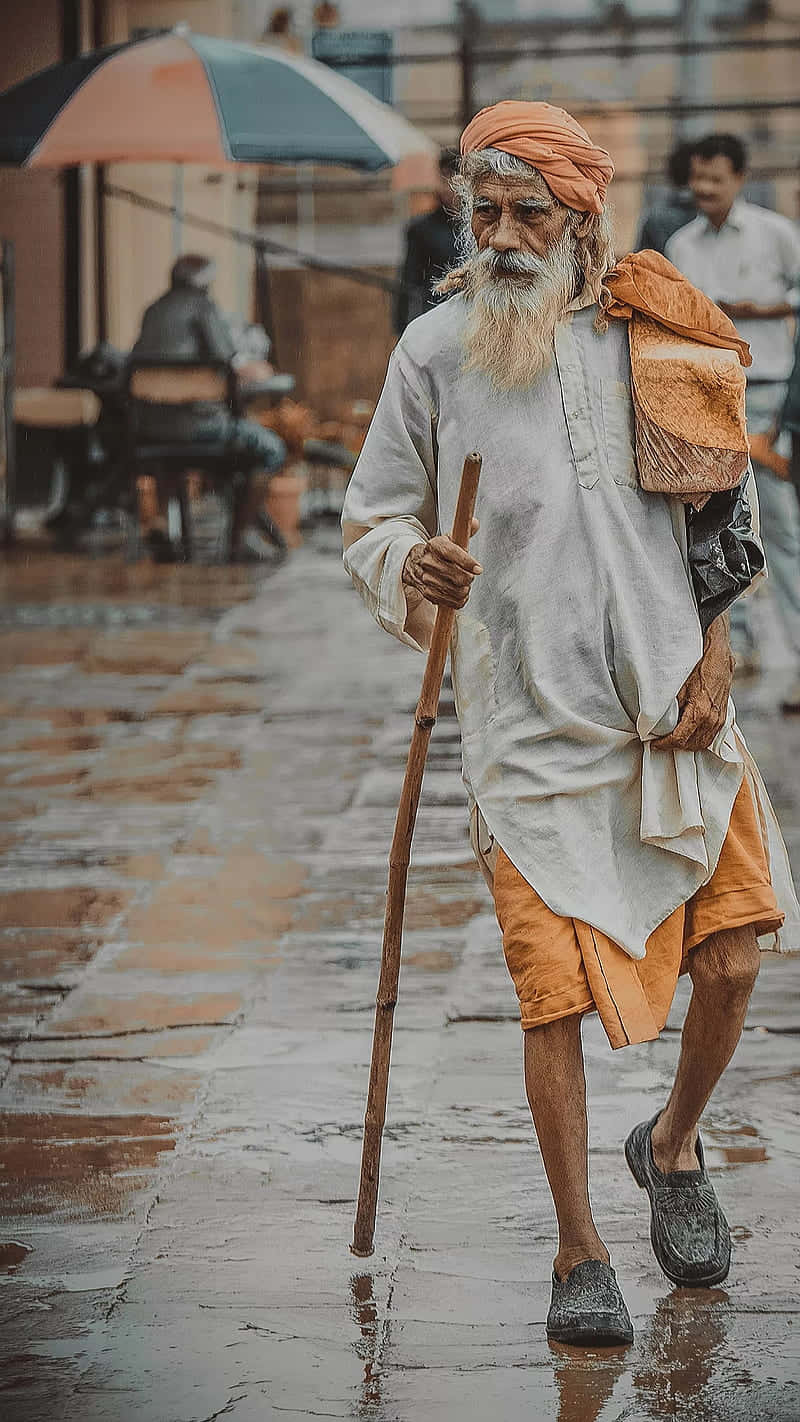 一位留著長長白鬍子的老人，手持木杖，走在濕漉漉的城市街道上。