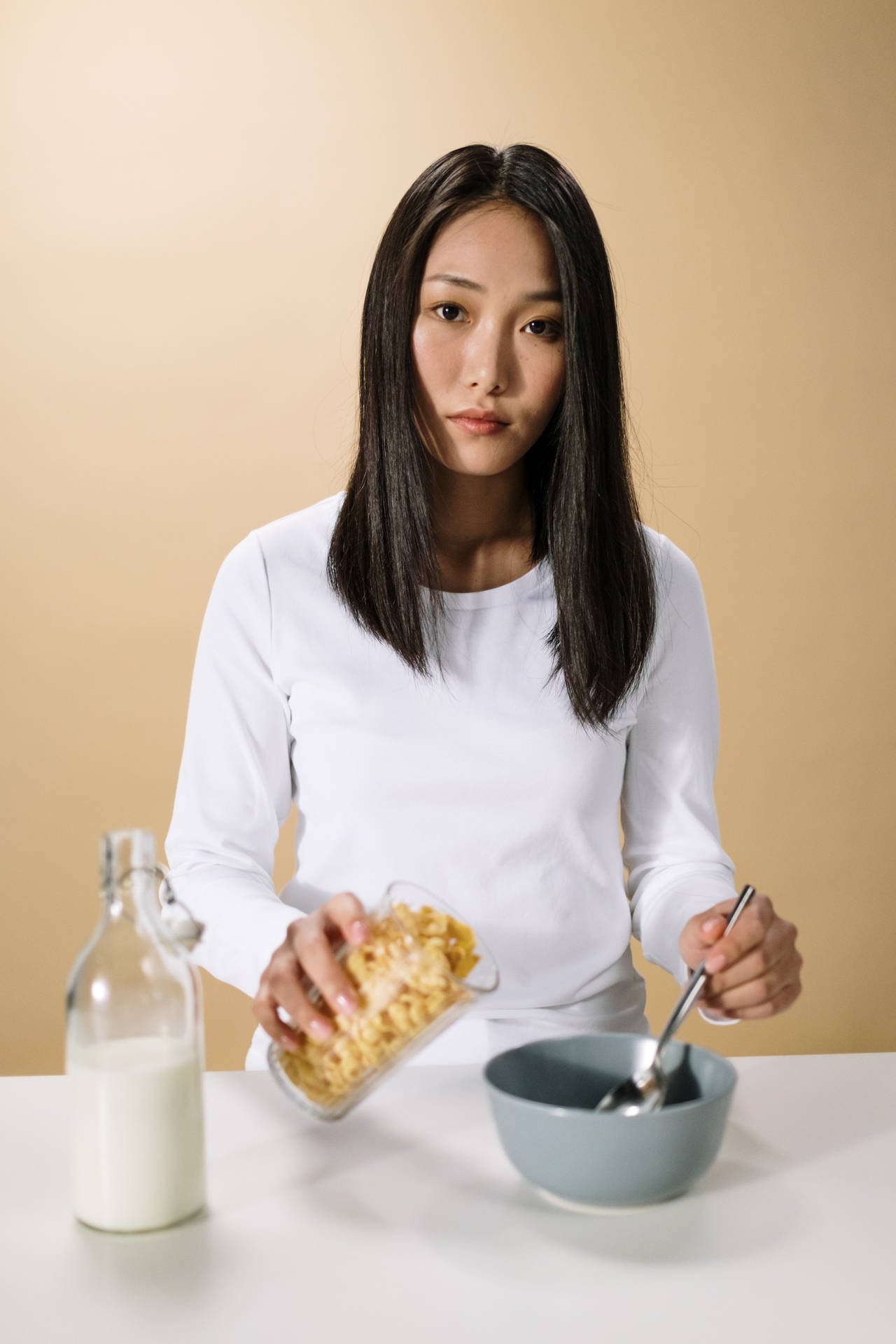 女性將穀物片倒入牛奶杯旁邊的碗中。