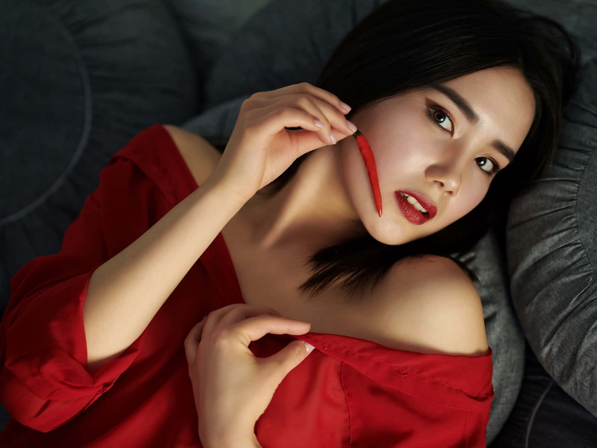 紅衣女性手持辣椒靠近臉頰躺在灰色沙發上