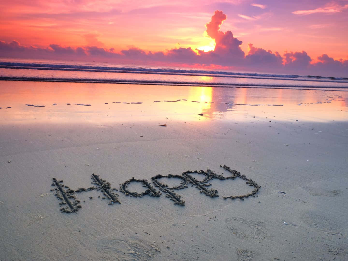 手持裝置顯示多個應用程式 壁紙 — 「happy」呢個字寫喺沙灘嘅沙上，日落時分有充滿活力嘅粉橙色天空同海浪。