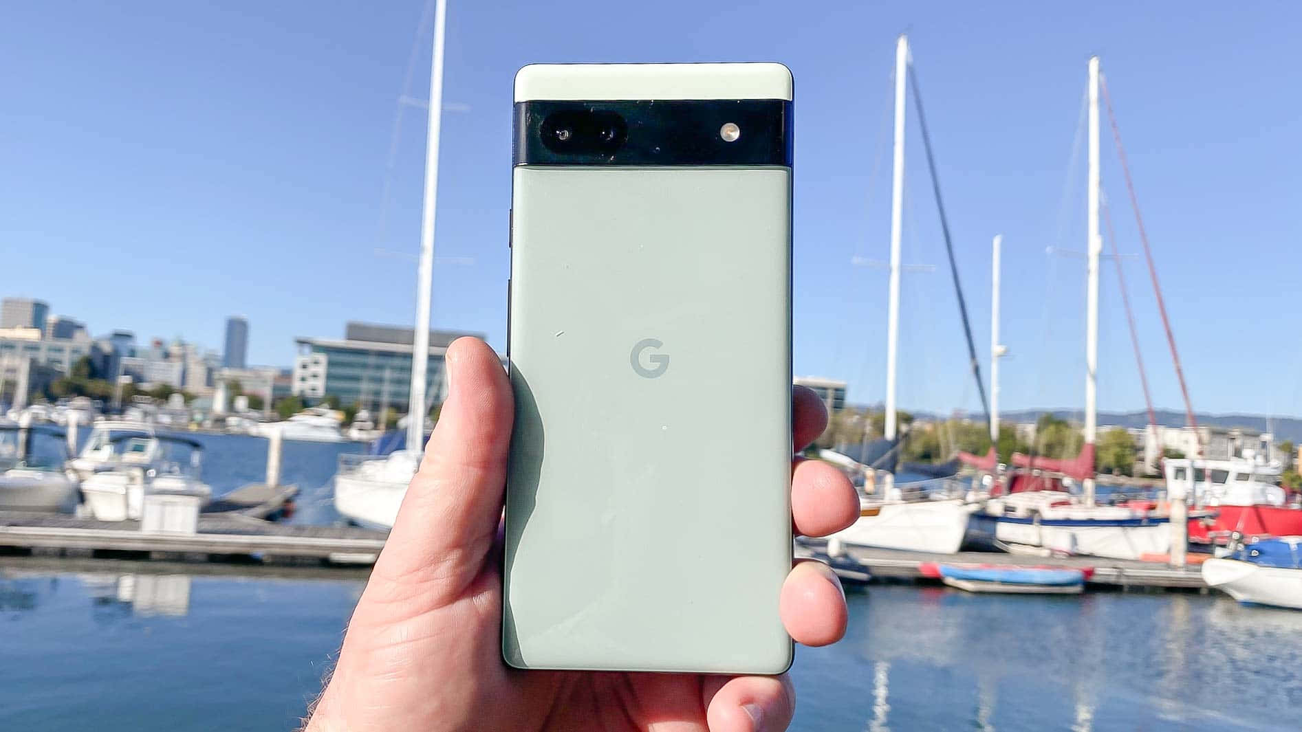 在碼頭拿著綠色 Google Pixel 手機，背景有船隻和城市建築。