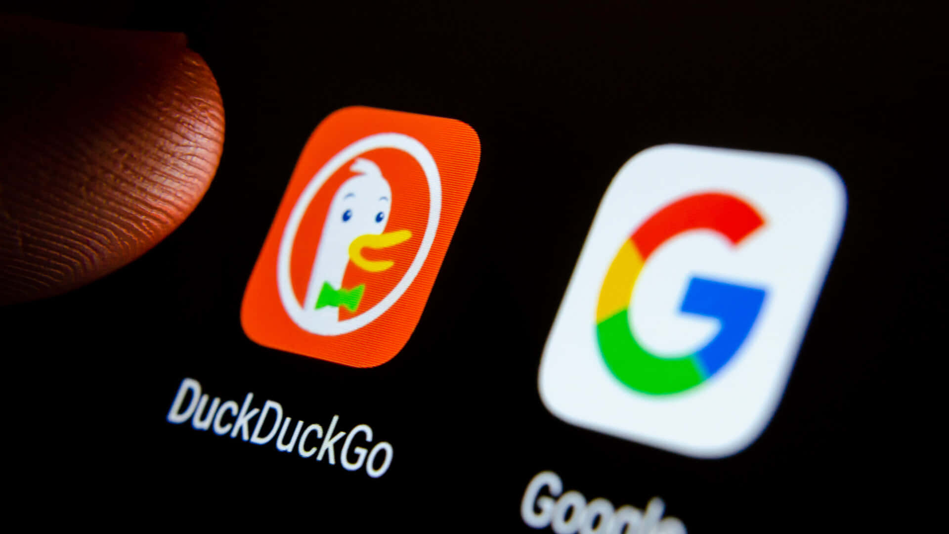 Duckduckgo 桌布 壁紙 — 手指懸浮在智能手機屏幕上Google旁邊的DuckDuckGo應用程式圖示上的特寫。