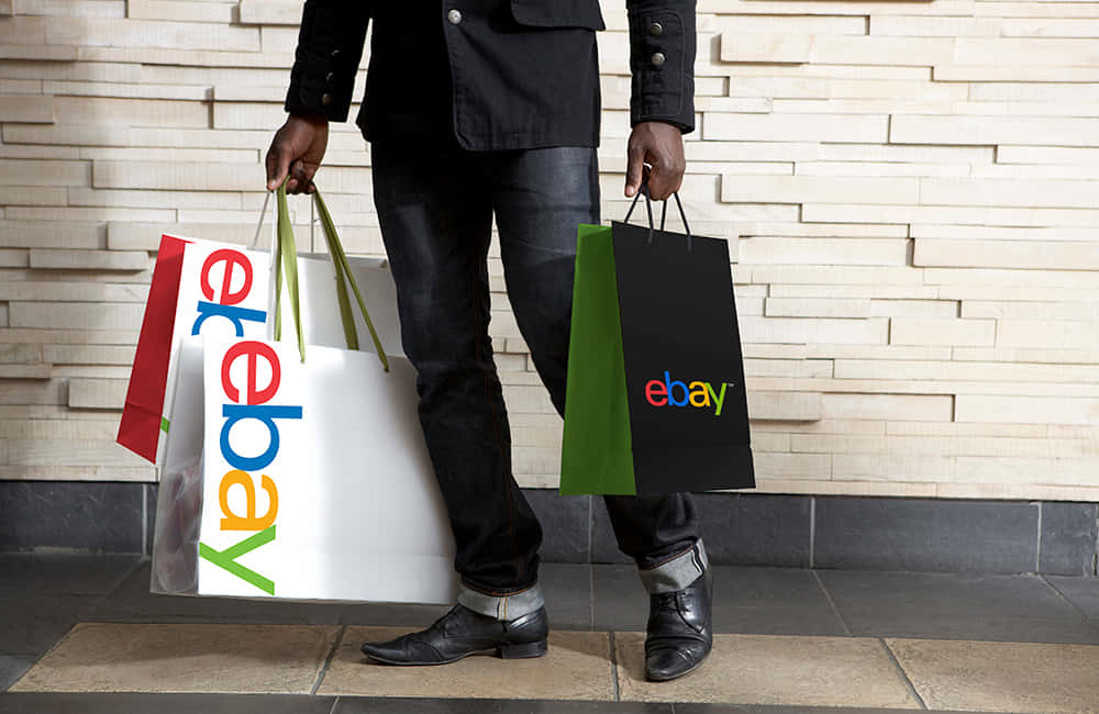 手提袋印有 eBay UK 標誌的男子 壁紙 — 一名身穿深色衣服的人手持多個色彩繽紛的eBay購物袋，靠著現代紋理牆。